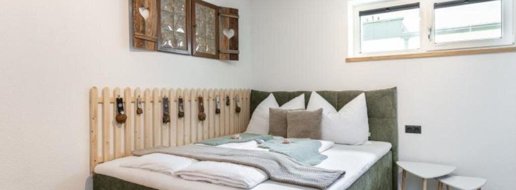 A modern bedroom with a comfortable bed and harmonious colors. The walls are simple and bright, with decorative elements made of wood. - Apartment DoLa - Längenfeld