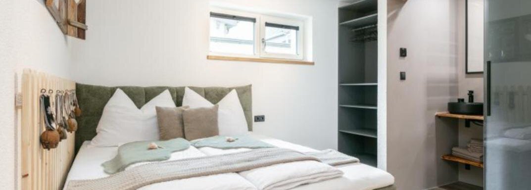A cozy bedroom with a soft bed and modern furnishings. The room is bright and inviting, with a practical wardrobe and an adjoining bathroom. - Apartment DoLa - Längenfeld