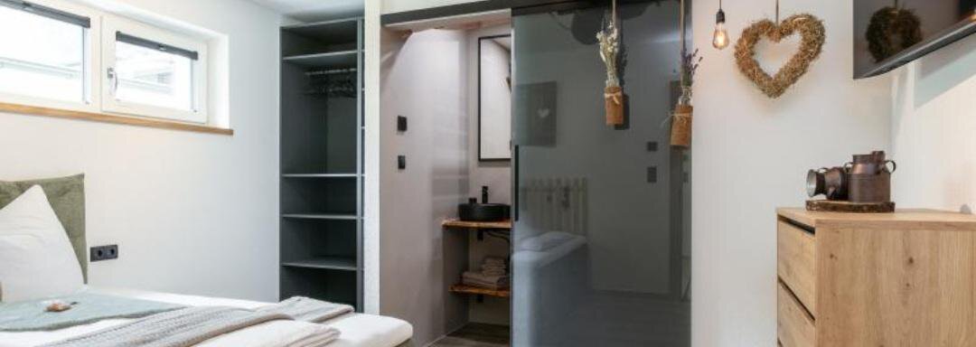 A modern bedroom with a comfortable bed and a wooden wardrobe. The room has a bright, inviting atmosphere and an open connection to the bathroom. - Apartment DoLa - Längenfeld