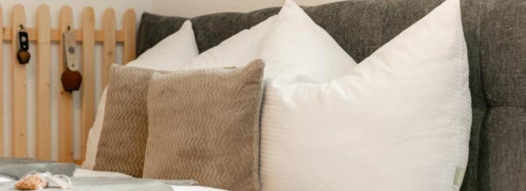 A cozy bed with several pillows in different colors. In the background, wooden paneling can be seen. - Apartment DoLa - Längenfeld
