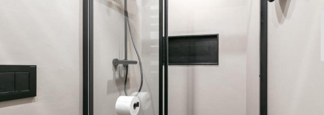 A modern shower with glass walls and a simple design. The wall is light grey, and there is a holder for toilet paper. - Apartment DoLa - Längenfeld