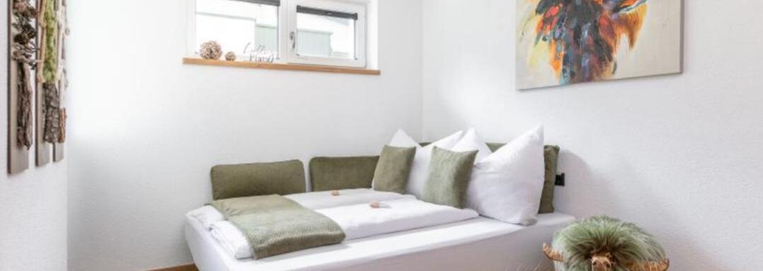 A bright and modern apartment with a cozy bed and colorful artwork on the wall. The floor is made of wood and the windows let in a lot of light. - Apartment DoLa - Längenfeld