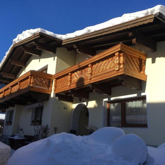 A cozy house with wooden balconies, surrounded by snowy ground. In the background, alpine mountains and blue sky are visible. - Apartment Josef Gstrein - Längenfeld