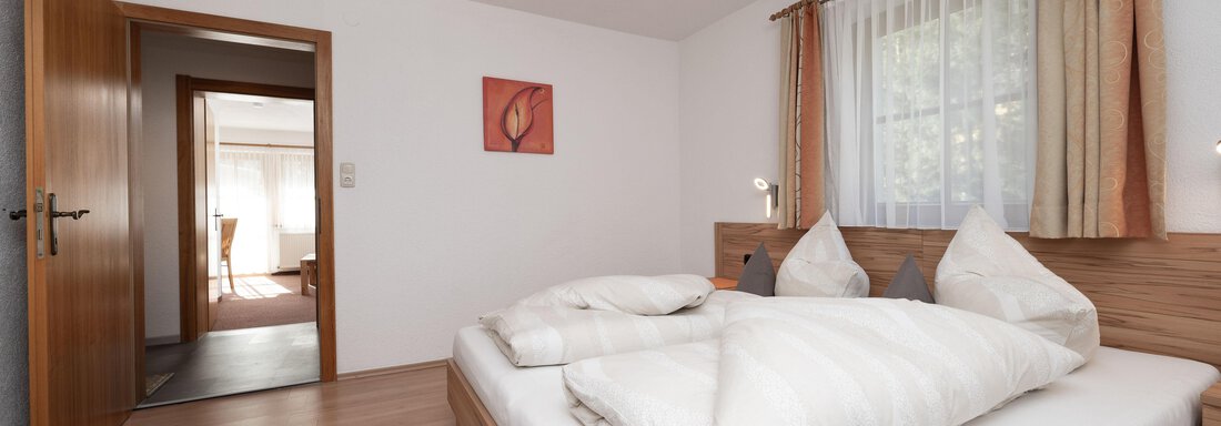 Ein gemütliches Schlafzimmer mit einem Doppelbett und bequemen Kissen. Der Raum hat helle Wände und ein Fenster mit Vorhängen. - Appart Klotz Alpenglück - Längenfeld