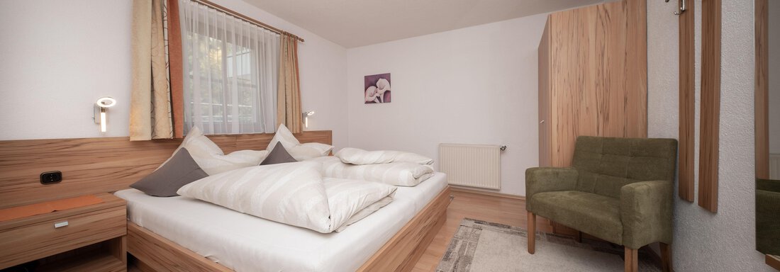 Ein modernes Schlafzimmer mit einem Doppelbett und großen Kissen. Ein gemütlicher Sessel und ein heller Teppich vervollständigen die Einrichtung. - Appart Klotz Alpenglück - Längenfeld