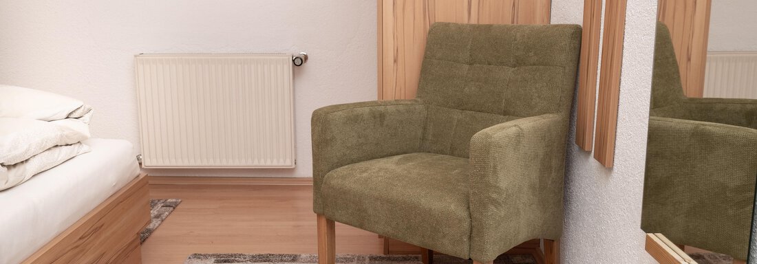 Ein gemütlicher Raum mit einem Bett und einem grünen Sessel. An der Wand befindet sich ein Spiegel und das Zimmer ist hell und modern eingerichtet. - Appart Klotz Alpenglück - Längenfeld