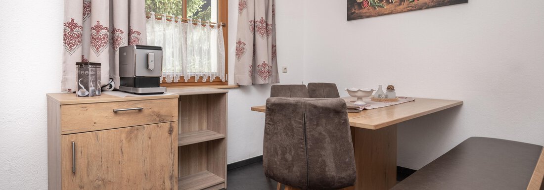 Ein gemütlicher Essbereich mit einem Holztisch, Stühlen und einem Fenster mit Vorhängen. Im Hintergrund hängt ein farbenfrohes Bild an der Wand. - Appart Klotz Alpenglück - Längenfeld