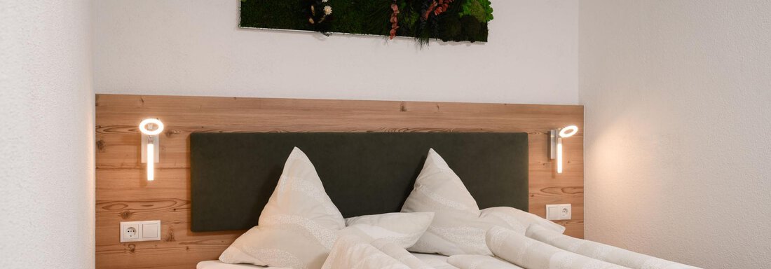 Ein gemütliches Schlafzimmer mit einem Doppelbett und zwei großen Kissen. An der Wand hängt ein grünes Kunstwerk aus Pflanzen. - Appart Klotz Alpenglück - Längenfeld