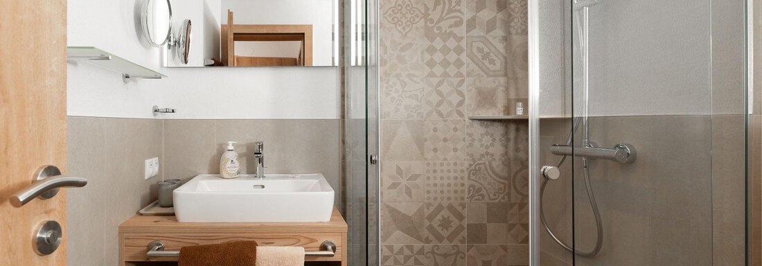 Ein modernes Badezimmer mit einer Dusche und einem Waschbecken. Die Wände sind hell und es gibt Holz- und Fliesenelemente für einen eleganten Look. - Appart Klotz Alpenglück - Längenfeld