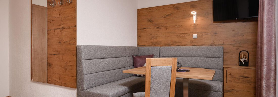 Ein moderner Essbereich mit einer gemütlichen Sitzgelegenheit und einem Holzschrank. An der Wand befindet sich ein Fernseher und ein Spiegel. - Appart Klotz Alpenglück - Längenfeld