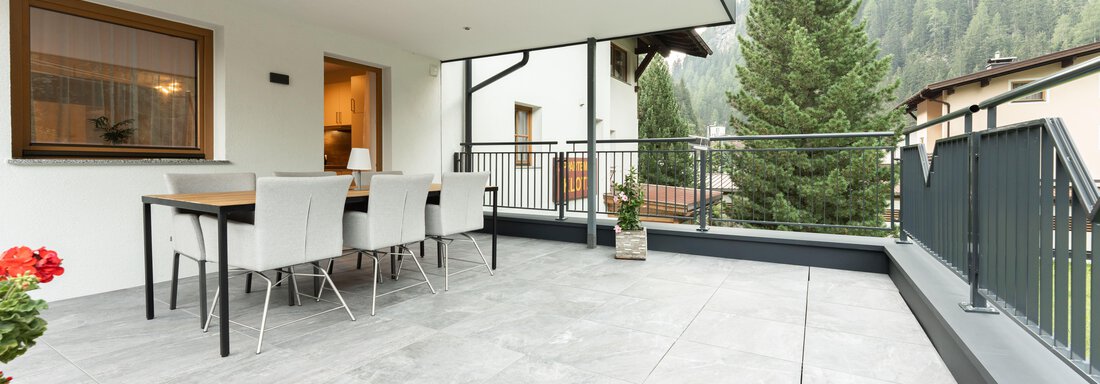 Eine moderne Terrasse mit einem Esstisch und mehreren Stühlen. Im Hintergrund sind grüne Bäume und Berge sichtbar. - Appart Klotz Alpenglück - Längenfeld