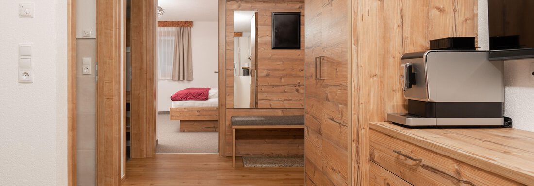 Ein heller Flur mit Holzverkleidung und einem Fenster. Im Hintergrund sieht man ein Schlafzimmer mit einem roten Bett. - Appart Klotz Alpenglück - Längenfeld