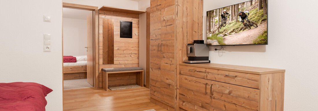 Ein modernes Zimmer mit Holzmöbeln und einem gemütlichen Bett. An der Wand hängt ein Fernseher, der eine Outdoor-Aktivität zeigt. - Appart Klotz Alpenglück - Längenfeld