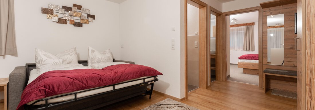 Ein gemütliches Schlafzimmer mit einem Bett und roten Decken. Die Wände sind in hellen Tönen gehalten und es gibt einen schönen Teppich auf dem Boden. - Appart Klotz Alpenglück - Längenfeld