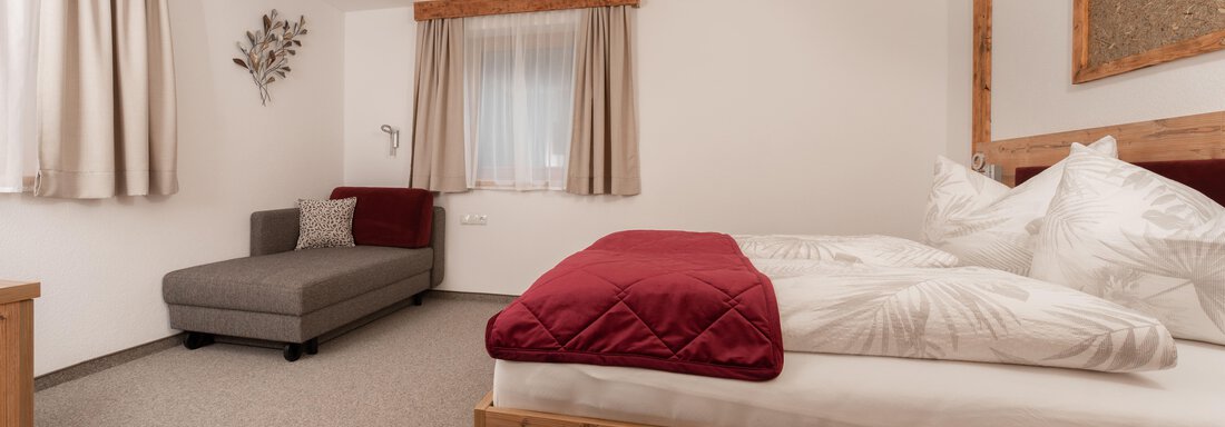 Ein gemütliches Zimmer mit einem großen Bett und einem modernen Schlafsofa. Die Wände sind hell und es gibt große Fenster mit Vorhängen. - Appart Klotz Alpenglück - Längenfeld