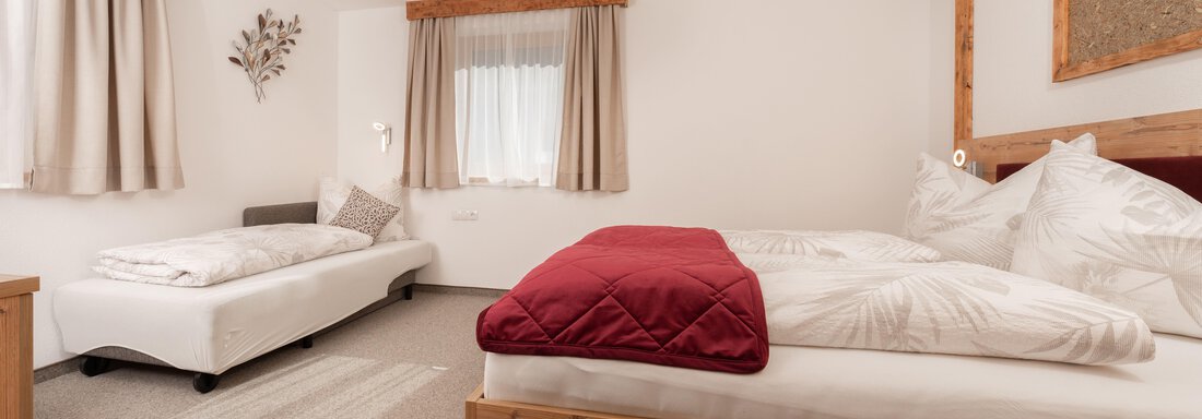 Ein gemütliches Schlafzimmer mit Holzbetten und einem Tagesbett. Die Wände sind in neutralen Farben gehalten, und die Fenster lassen viel Licht herein. - Appart Klotz Alpenglück - Längenfeld