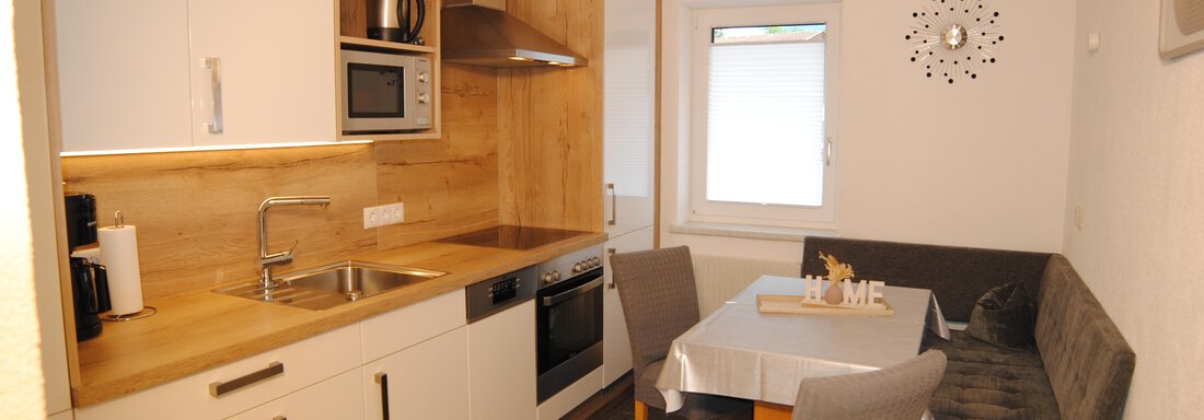A modern kitchen with wooden details and white cabinets.  
The room is bright and inviting with a dining area. - Appart Tanja - Längenfeld