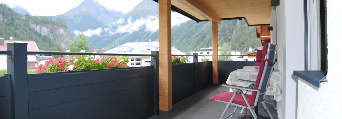 A spacious balcony with a view of the mountains. On the balcony, there is a cozy seating area with blooming plants in the background. - Appart Tanja - Längenfeld