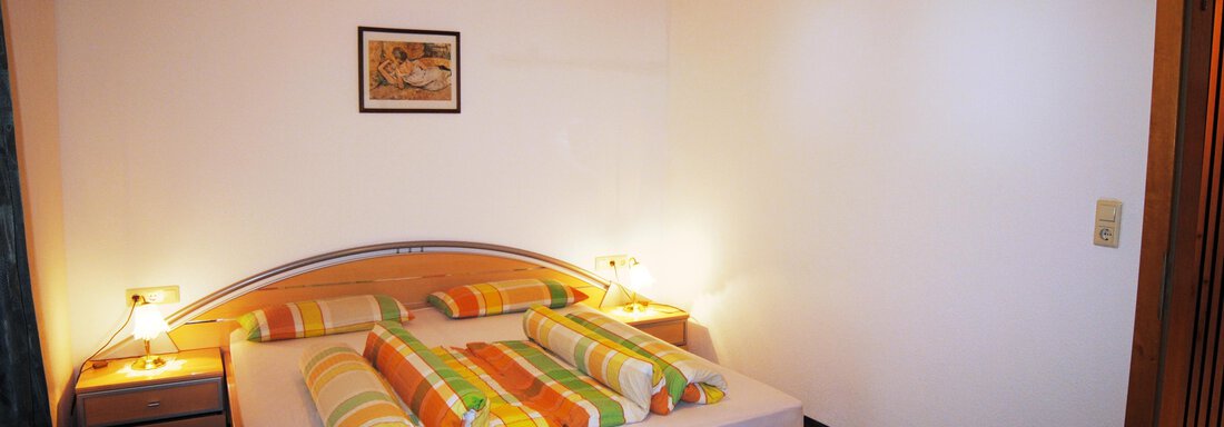 A cozy bedroom with a double bed. The walls are light, and the wooden ceiling creates a warm atmosphere. - Appart Tanja - Längenfeld