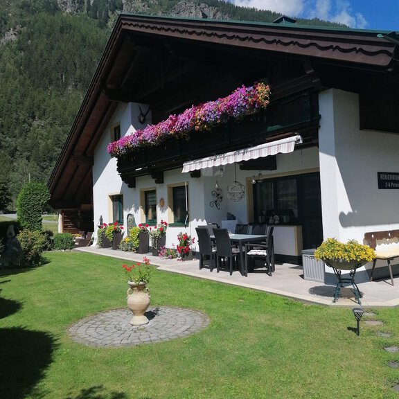 A pretty house with a well-kept garden and blooming plants. In the background, green mountains and a blue sky can be seen. - Appt. Gritsch Marlies - Längenfeld