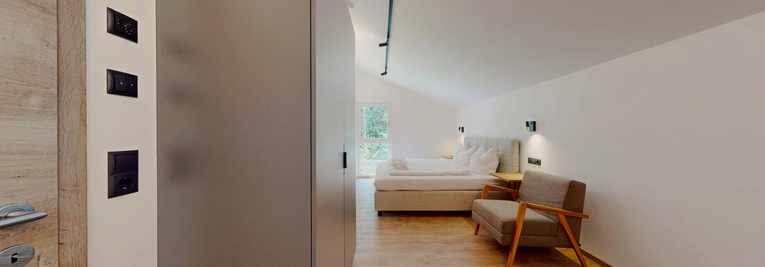 Ein modernes Zimmer mit einem hellen Holzfußboden. Es gibt ein Bett und einen Sessel, sowie angenehmes Licht von den Wänden. - Das Berg Loft - Längenfeld