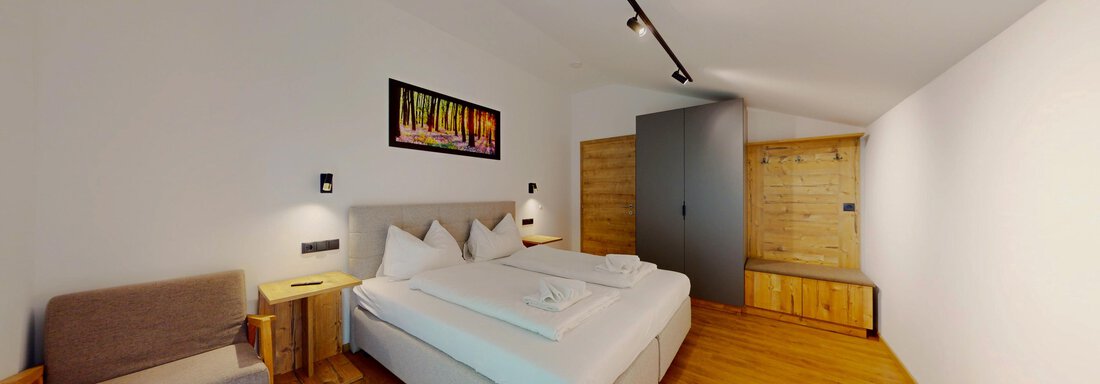 Ein modernes Schlafzimmer mit einem großen Bett und minimalistischer Einrichtung. Der Raum ist hell und freundlich mit Holzfußboden und einer gemütlichen Sitzecke. - Das Berg Loft - Längenfeld