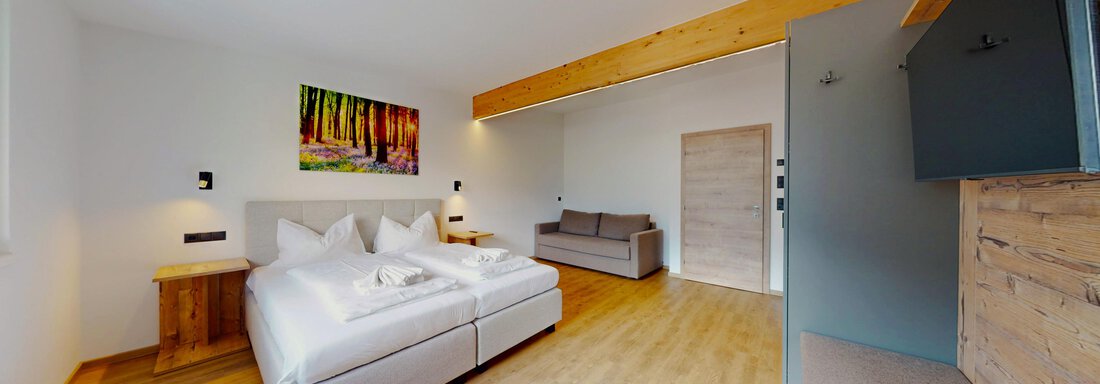 Ein modernes Zimmer mit Doppelbett und einem Sofa. Holzaccents und ein großes Fenster sorgen für ein helles und einladendes Ambiente. - Das Berg Loft - Längenfeld