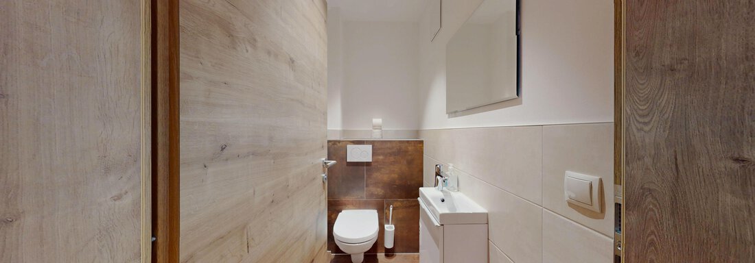 Ein modernes Badezimmer mit Holz- und Fliesenakzenten. Es enthält eine Toilette, ein Waschbecken und einen großen Spiegel. - Das Berg Loft - Längenfeld