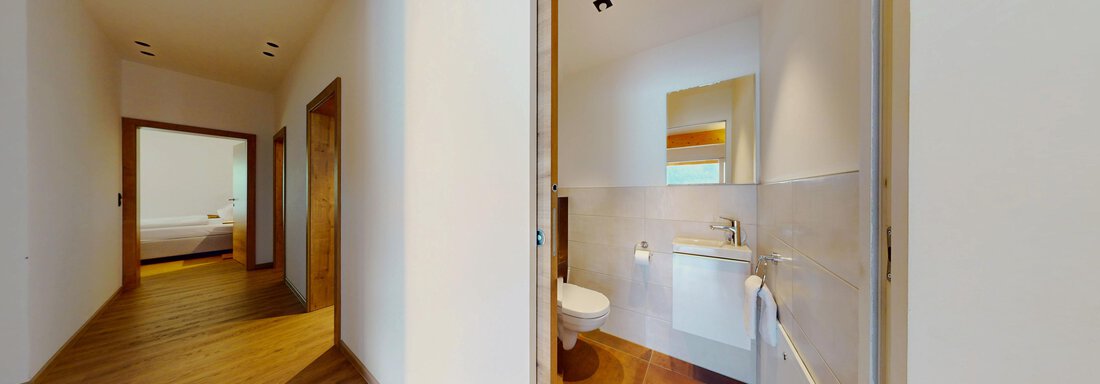 Ein moderner Flur mit einem Blick auf ein Badezimmer. Der Raum hat helle Wände und einen Holzfußboden. - Das Berg Loft - Längenfeld