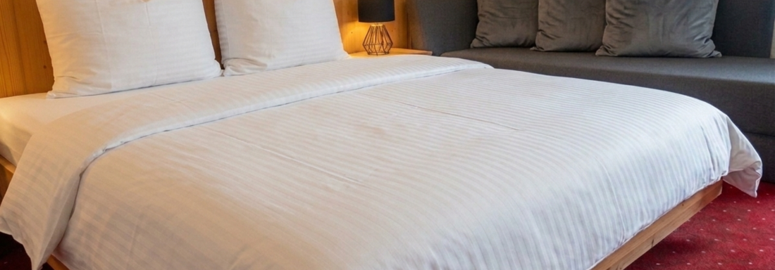 Ein gemütliches Schlafzimmer mit einem großen Bett und zwei höheren Kopfkissen. Neben dem Bett befindet sich eine graue Couch mit Kissen. - Ferienhaus Schrankogelblick - Längenfeld