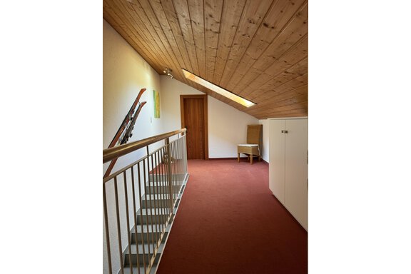Ein heller Flur mit Holzdecke und rotem Teppich. An der Wand lehnen Skier, und eine Tür führt zu einem weiteren Raum. - Ferienhaus Volgger - Längenfeld