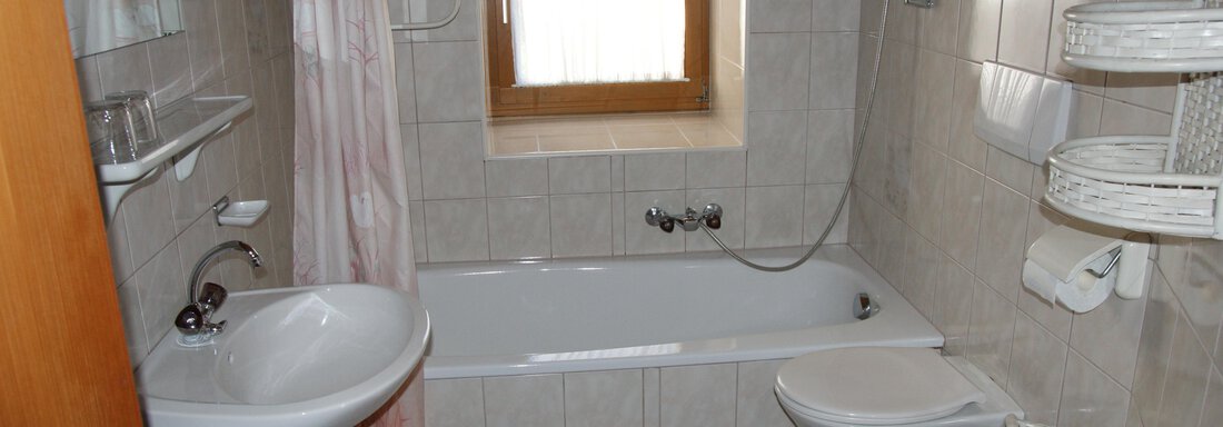 Ein helles Badezimmer mit einer Badewanne, Dusche und Waschbecken. Die Wände sind gefliest und es gibt ein Fenster, das natürliches Licht hineinlässt. - Ferienhaus Volgger - Längenfeld