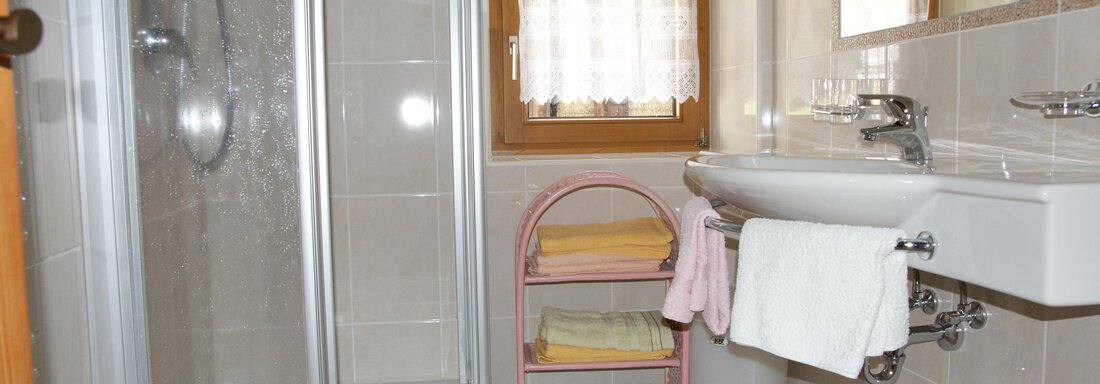 Ein helles Badezimmer mit einer Dusche und einem Waschbecken. Handtücher in verschiedenen Farben sind ordentlich gestapelt. - Ferienhaus Volgger - Längenfeld