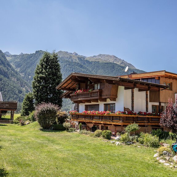 Ein schönes Holzhaus in einer malerischen Landschaft. Im Hintergrund sind hohe Berge und ein klarer Himmel zu sehen. - Gästehaus Waltraud - Längenfeld