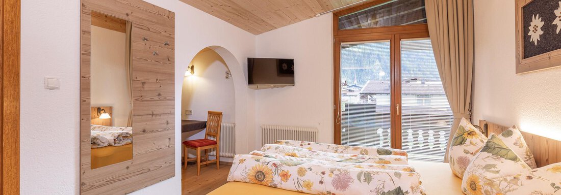 A cozy room with a large window and a view of the mountains. The decor is modern, with a wooden ceiling and a simple, warm color scheme. - Gästehaus Waltraud - Längenfeld
