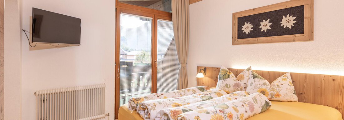 A cozy bedroom with a large bed and balcony. There is a television and windows overlooking the outside. - Gästehaus Waltraud - Längenfeld