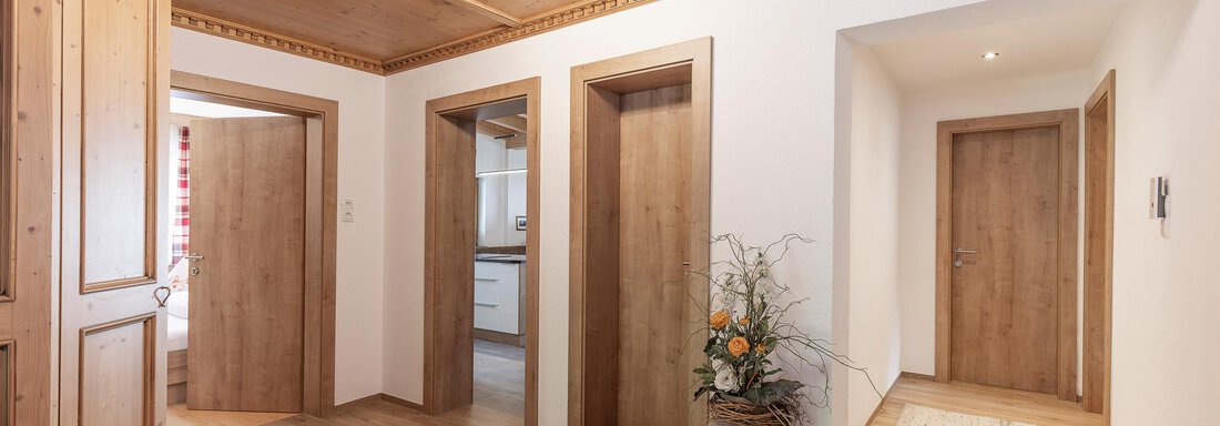 A bright hallway with wood paneling and several doors. A plant and a rug give the room a cozy atmosphere. - Gästehaus Waltraud - Längenfeld