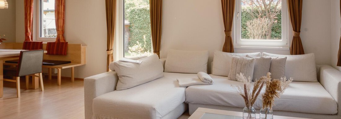 A modern living room with a cozy sofa and a coffee table. Large windows let in plenty of light and offer a view of the greenery. - Haus Margret - Längenfeld