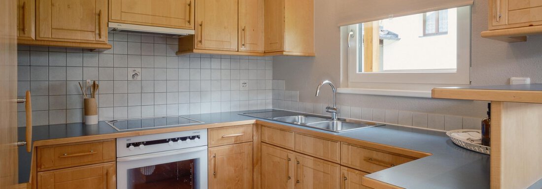 A modern kitchen with wooden cabinets and a window. The equipment includes a stove and a sink. - Haus Margret - Längenfeld