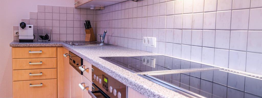 A modern kitchen with light wood cabinets and gray countertops. The equipment includes a stove, an oven, and a coffee machine. - Haus Viktoria - Längenfeld