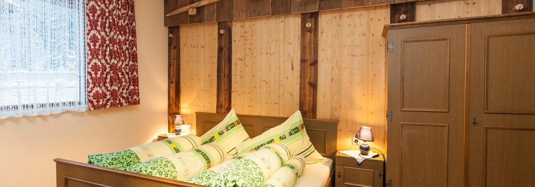 IMG_0746 A cozy bedroom with a wooden bed and colorful cushions. The walls are made of wood, and the room has a warm, inviting ambiance. - Haus Waldhof - Längenfeld