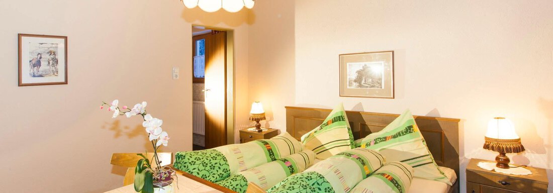 A cozy bedroom with two beds and green bedspreads. A table decoration with an orchid and diffuse lighting create a pleasant atmosphere. - Haus Waldhof - Längenfeld