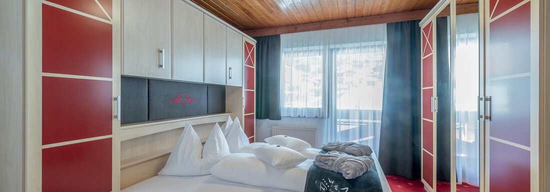 A cozy bedroom with a large bed and modern wooden furniture.  
Large windows let in plenty of light and create a warm atmosphere. - Hotel Burgstein alpin & lifestyle - Längenfeld