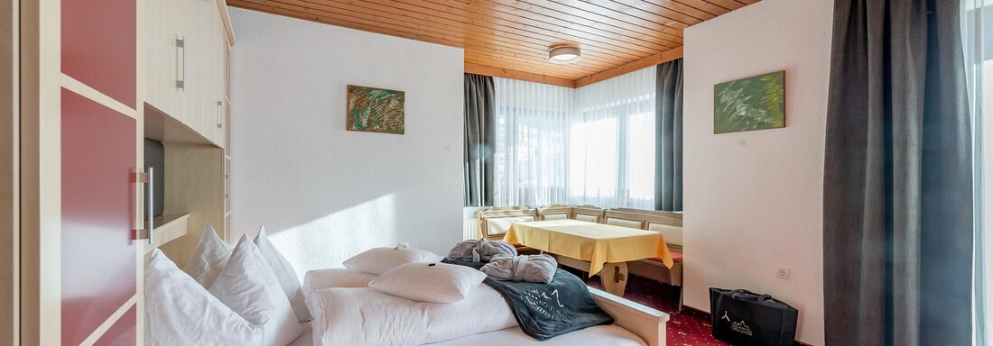 A cozy bedroom with wooden ceilings and a red carpet. There is a single bed and a dining area with a table and chairs. - Hotel Burgstein alpin & lifestyle - Längenfeld