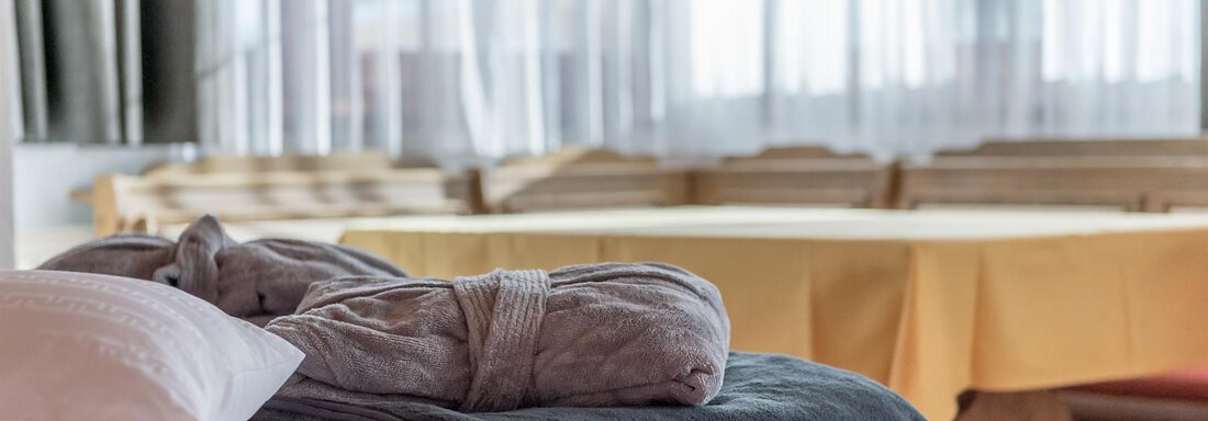 A cozy bed with a gray blanket and towel. In the background, tables and curtains create an inviting atmosphere. - Hotel Burgstein alpin & lifestyle - Längenfeld