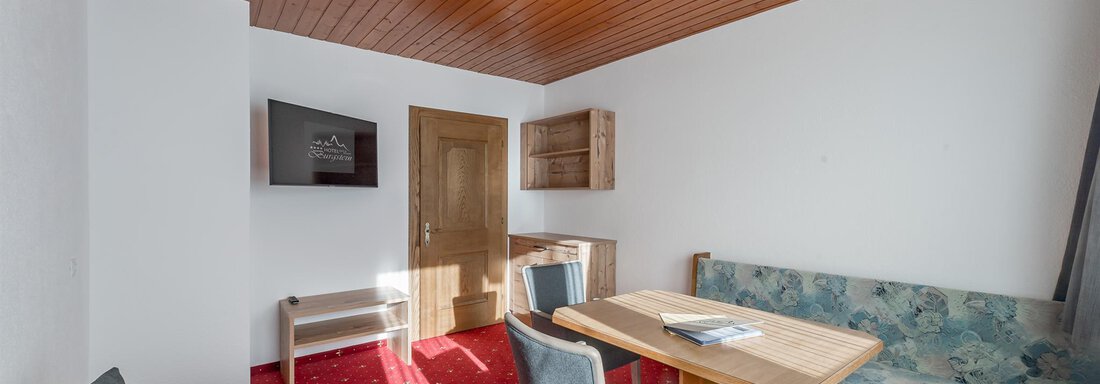 A cozy living space with a dining table and chairs. The walls are light, and there are wooden elements on the ceiling. - Hotel Burgstein alpin & lifestyle - Längenfeld