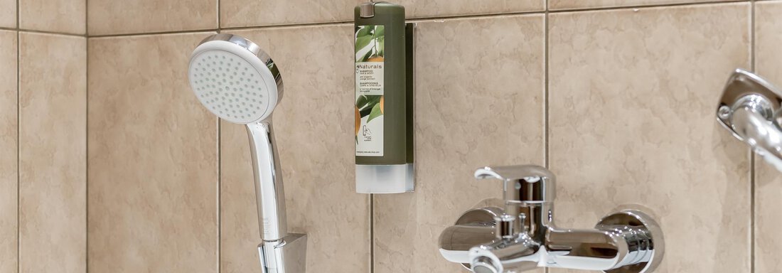 A modern bathroom with a showerhead and a faucet. On the wall, there is a dispenser for shower gel. - Hotel Burgstein alpin & lifestyle - Längenfeld
