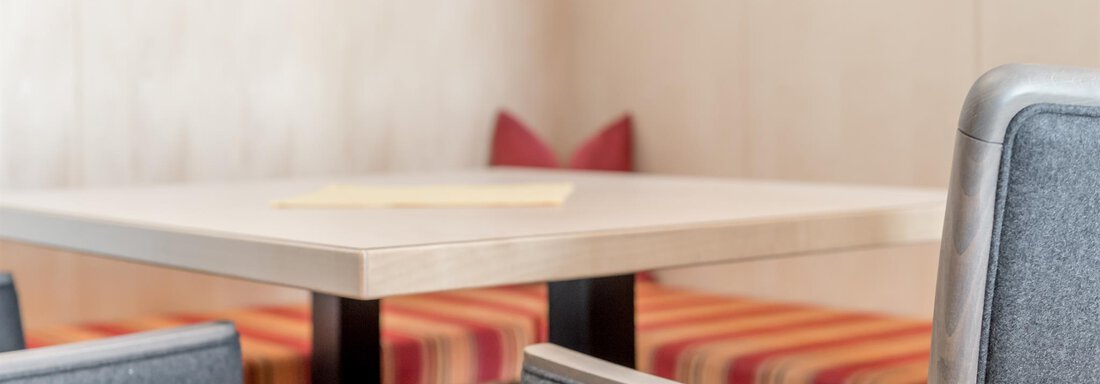 A modern table with light chairs in a cozy room. In the background, striped benches are visible. - Hotel Burgstein alpin & lifestyle - Längenfeld