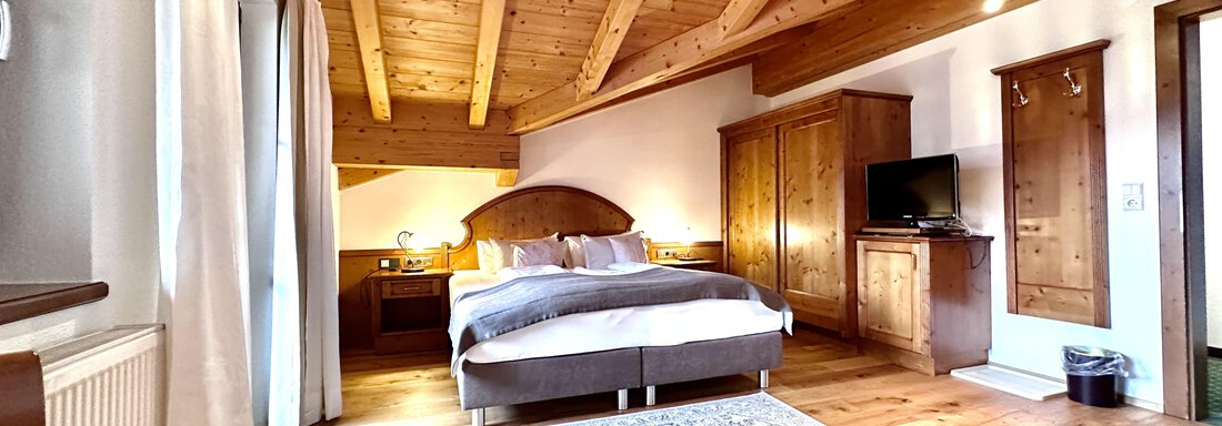 Ein gemütliches Zimmer mit Holzbalkendecke und einem großen Bett. Die warmen Holzmöbel und das natürliche Licht schaffen eine einladende Atmosphäre. - Hotel Stern - Längenfeld