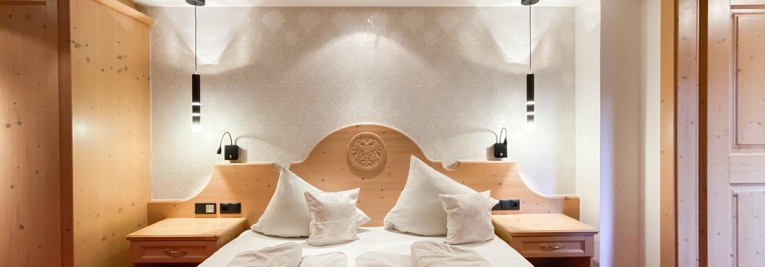 Ein stilvolles Hotelzimmer mit einem komfortablen Doppelbett und Holzvertäfelungen. Die sanfte Beleuchtung schafft eine entspannte Atmosphäre. - Hotel Stern - Längenfeld